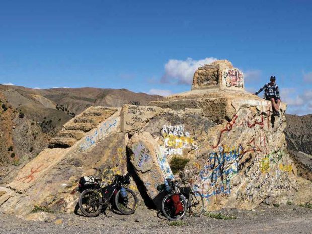 Kevan sitting on a marker identifying the peak of the Tizi n’Isli Pass while riding along the spine of the Atlas Mountains in Morocco in 2017.