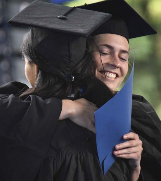 two new graduates sharing a congratulatory hug.