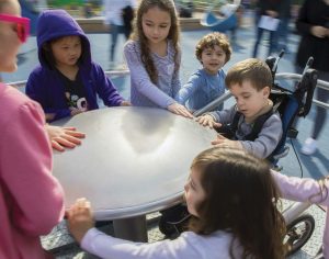 Children crowd onto the wheelchair-accessible spinning dish at the Magical Bridge playground.