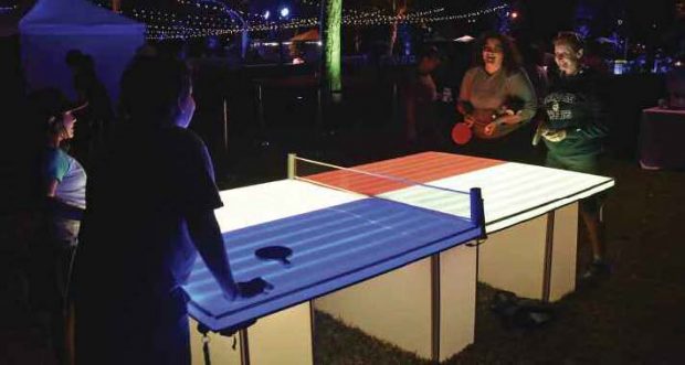 Partygoers enjoy a game of ping pong on a lighted table.