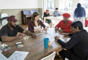 Project Horseshoe Farm fellow Greta Hartmann (second from left) plays dominos with adults in the community center on Greensboro's Main Avenue