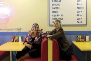 Wendy Molyneux (left) and her sister Lizzie Molyneux-Logelin chat in a working replica of the diner in Bob’s Burgers.