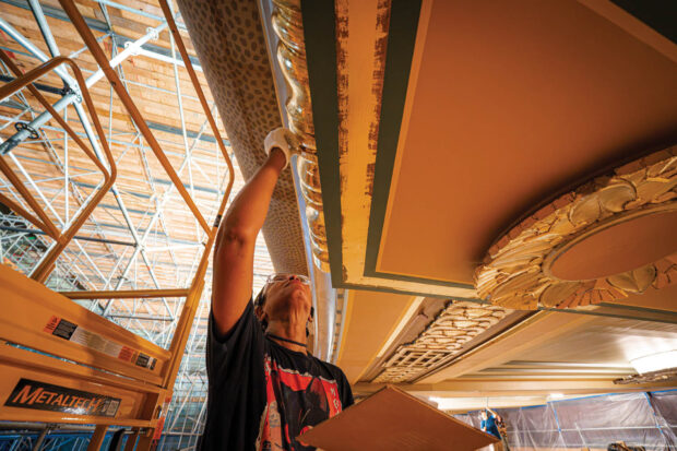 Woman applying gold leaf to the underside of a balcony